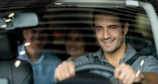 A driver smiling behind the wheel with riders in the back seat