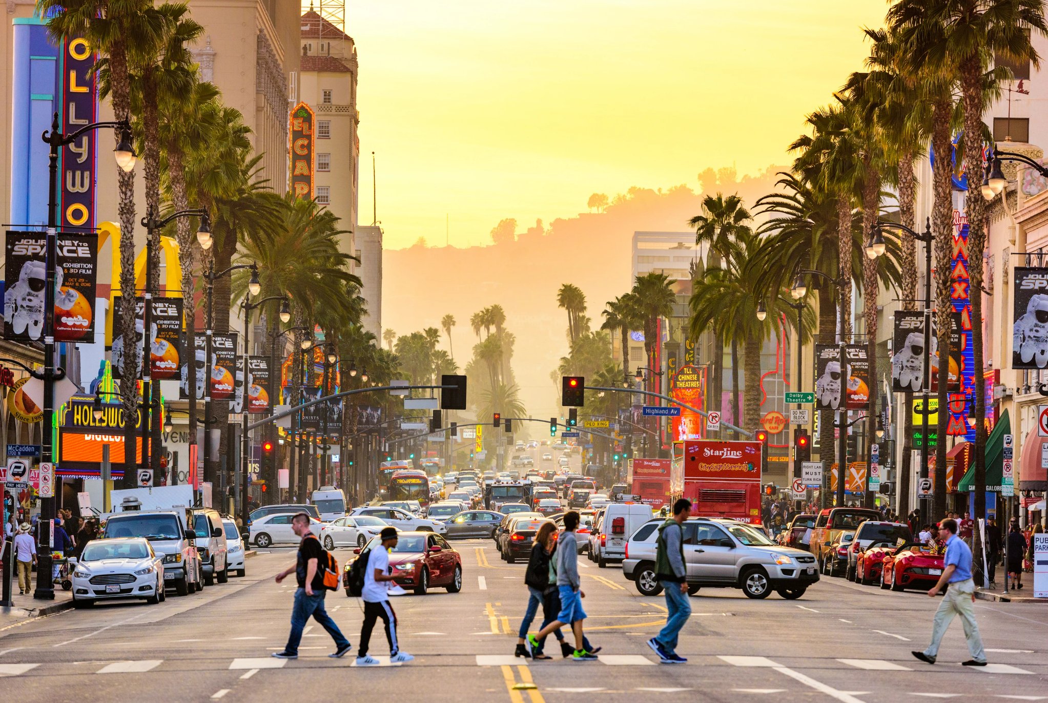 Hollywood Boulevard at sunset with pedestrians crossing and palm trees lining the street