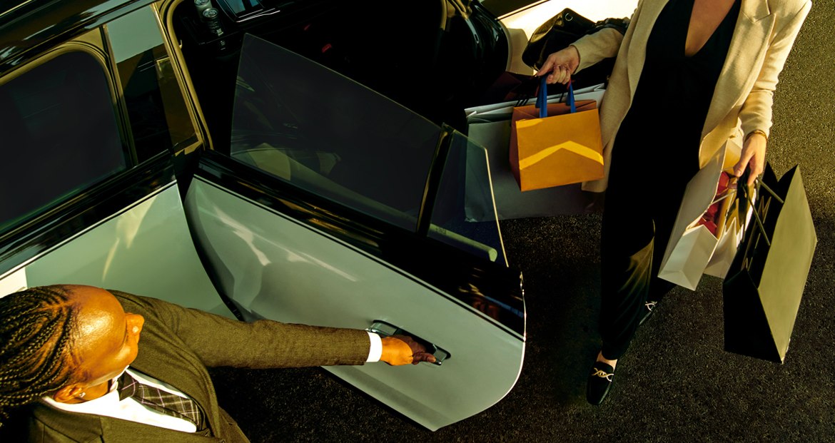 A chauffeur opening the car door for a rider carrying shopping bags